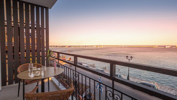 A balcony with wicker chairs and a table, overlooking a waterfront with boats and a bridge. - PORT VIEW (Zakynthos)