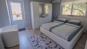 Un dormitorio con cama, una silla, armario, espejo y ventana.