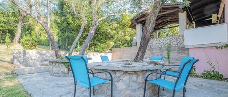 An outdoor patio with stone flooring and blue chairs around a central stone table.