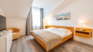 Ein Schlafzimmer mit Bett, Nachttischen, einer Lampe, einem Gemälde und einem Fenster mit Vorhängen.