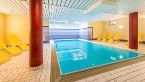 Ein Hallenbad mit gelben Liegestühlen und roten Säulen.