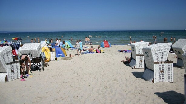 Ein Strand mit weißen Korbstühlen, Sonnenschirmen und Blick auf den Ozean.