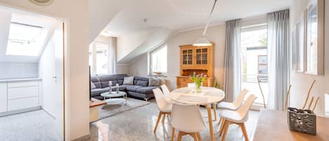 A modern living room with a dining area, a sofa, a wooden cabinet, and a clock on the wall.