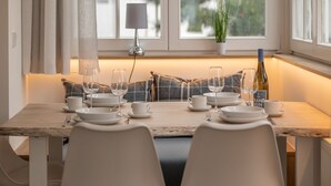 A dining area with a wooden table set for two, white chairs, and a potted plant on the windowsill. - Vacation apartment Sabei Villa Metropol, fireplace, sauna, close to the beach, beach chair (Binz)