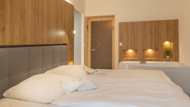 A modern hotel room with a large bed, a wooden headboard, a built-in bench, a small seating area, and a bathroom with a bathtub and a mirror. - Vacation apartment Sabei Villa Metropol, fireplace, sauna, close to the beach, beach chair (Binz)