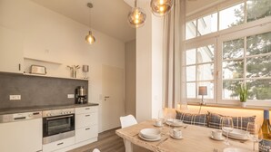 A modern kitchen with a dining area, featuring a wooden table, white chairs, and a view of trees through large windows. - Vacation apartment Sabei Villa Metropol, fireplace, sauna, close to the beach, beach chair (Binz)