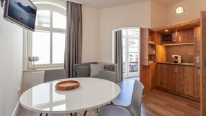 A modern living room with a round dining table, grey sofas, a flat-screen TV, and a kitchen area with wooden cabinets and a microwave. - Comfort apartment Wabi Sabi in the Villa Glückspilz for 4 people, beach location (Binz)