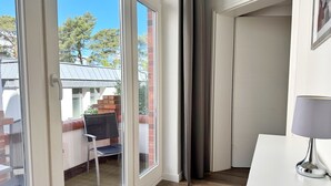 A room with a sliding glass door leading to an outdoor area with a chair and a table. There is a white desk with a lamp in the corner. - Comfort apartment Wabi Sabi in the Villa Glückspilz for 4 people, beach location (Binz)