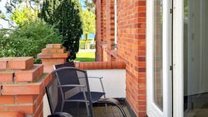 A brick exterior wall with a glass door, a metal chair, and a small brick structure. - Comfort apartment Wabi Sabi in the Villa Glückspilz for 4 people, beach location (Binz)