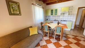 A cozy living room with a sofa and a dining table, a kitchen with green cabinets, and a checkered floor. - Apartman Villa Ljiljana 9 (Jadranovo)