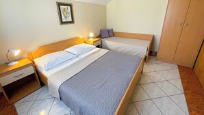 A bedroom with two beds, a nightstand with a lamp, a wardrobe, and a framed botanical print on the wall. - Apartman Villa Ljiljana 9 (Jadranovo)