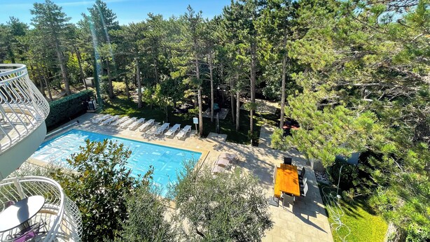 A pool area with lounge chairs and a wooden table, surrounded by trees and greenery. - Apartman Villa Ljiljana 9 (Jadranovo)