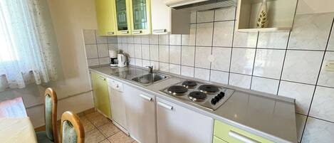 A compact kitchen with a stove, sink, and green cabinets.