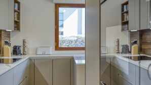 Une cuisine moderne avec des armoires blanches, un four encastré et une fenêtre donnant sur un immeuble.