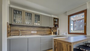 Une cuisine moderne avec des meubles gris, un pare-feu en bois et un îlot central intégré avec des tabourets de bar.