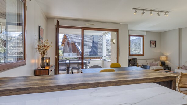 Une cuisine moderne dotée d’un grand plan de travail en marbre, de meubles en bois et d’un coin repas avec une chaise jaune.