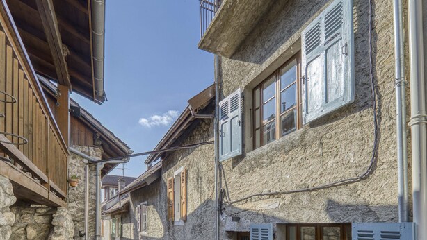 Une rue étroite bordée d’immeubles en pierre, de balcons en bois et de volets métalliques.