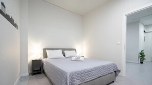 Une chambre à coucher au style minimaliste, avec un grand lit, une table de chevet et une petite table d’appoint.