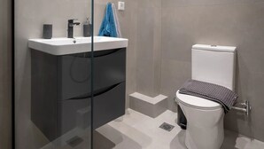 Une salle de bain moderne avec une paroi en verre, un miroir rond, un lavabo blanc et des toilettes.
