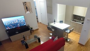A modern living room with a red sofa, a glass coffee table, a TV displaying a cityscape, and a kitchen area with a sink and cabinets. - La Casa di Lollo - Everything You Need Just Steps from the City Center (Firenze)