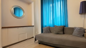 Une pièce avec un canapé, une lampe, une fenêtre avec des rideaux bleus et un miroir rond accroché au mur.