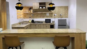 A modern kitchen with a central island, two bar stools, wooden cabinets, and pendant lighting. - Me Time Residence (Enugu)
