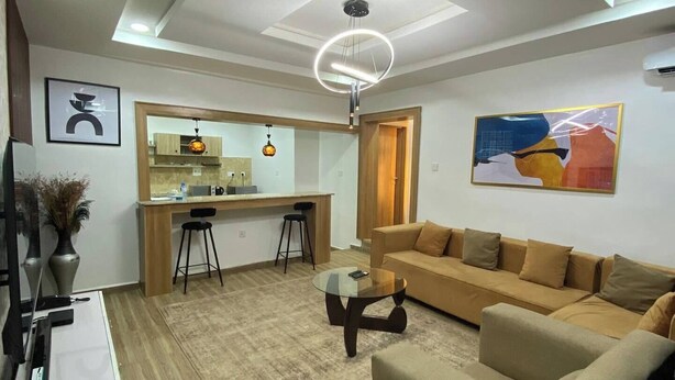 A modern living room with a sofa, coffee table, and a kitchen area with stools. - Me Time Residence (Enugu)