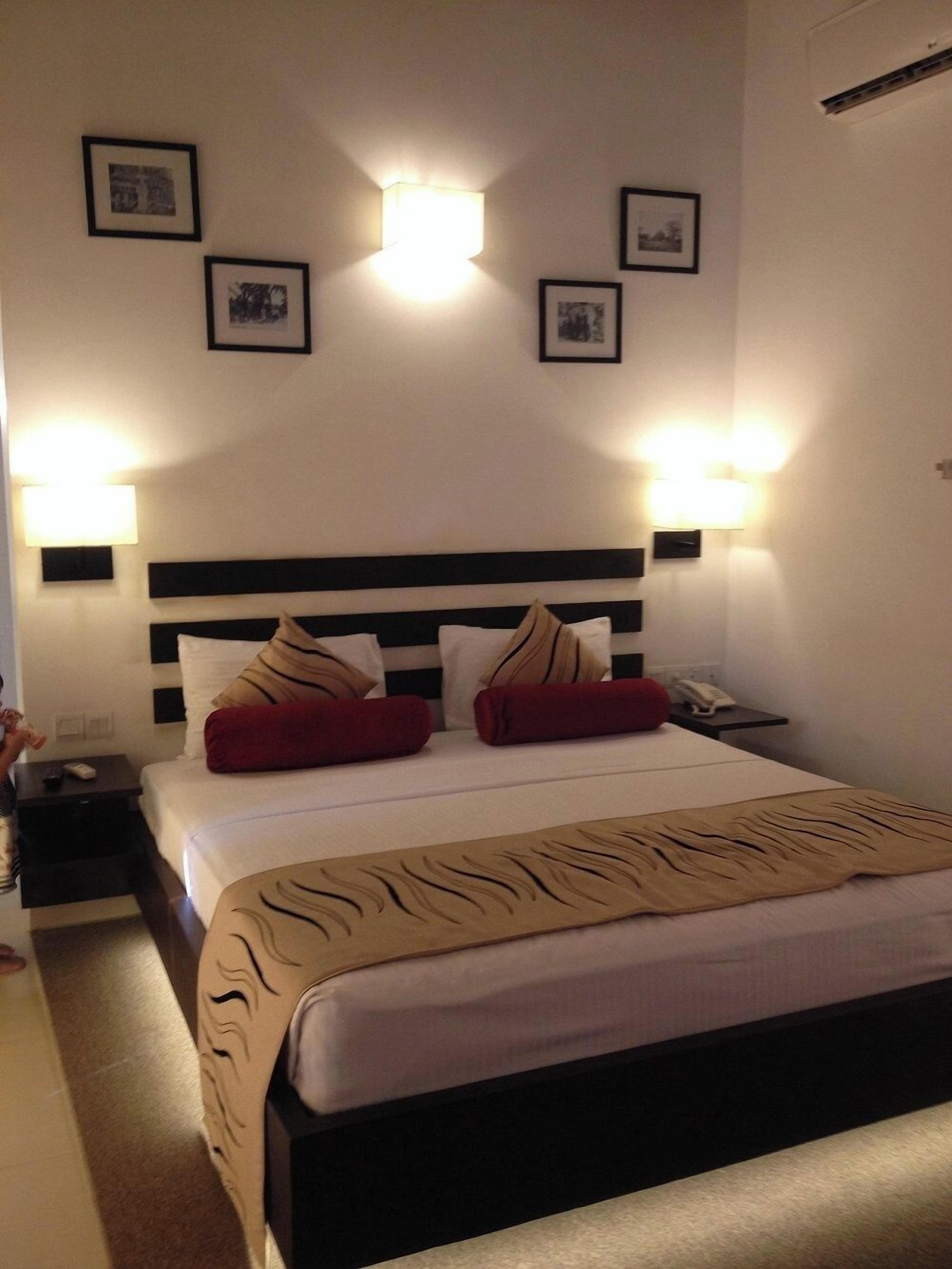 A hotel room with a large bed, two bedside tables, a nightstand, and wall-mounted lights.