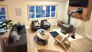 Un salón amplio con techo alto, ventanas grandes, chimenea y televisor de pantalla plana montado en la pared.