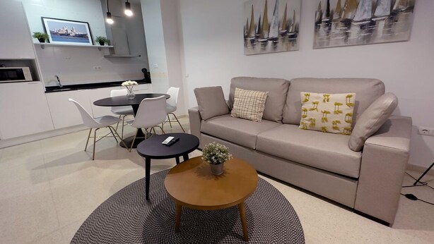 Un salon moderne avec un canapé beige, une table basse ronde et un coin repas comprenant une petite table et des chaises.