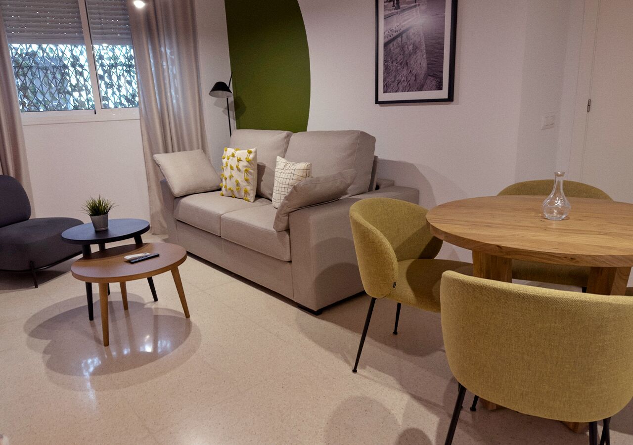 Una sala de estar con un sofá, dos sillones, una mesita pequeña y una mesa redonda con sillas.
