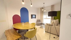 Un salon moderne avec une table ronde en bois, des chaises jaunes, un canapé gris et un lampadaire noir.