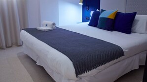 Un lit bien fait, avec une couette blanche, un plaid bleu foncé et une serviette blanche posée sur le côté.