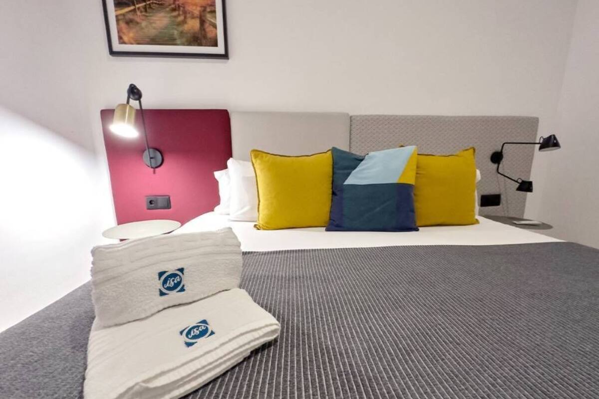 Une chambre d’hôtel avec un lit, des oreillers, une lampe de chevet et une serviette pliée.