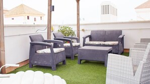 Un espace extérieur aménagé avec des meubles en osier et une petite table, le tout entouré d’une pergola en bois.