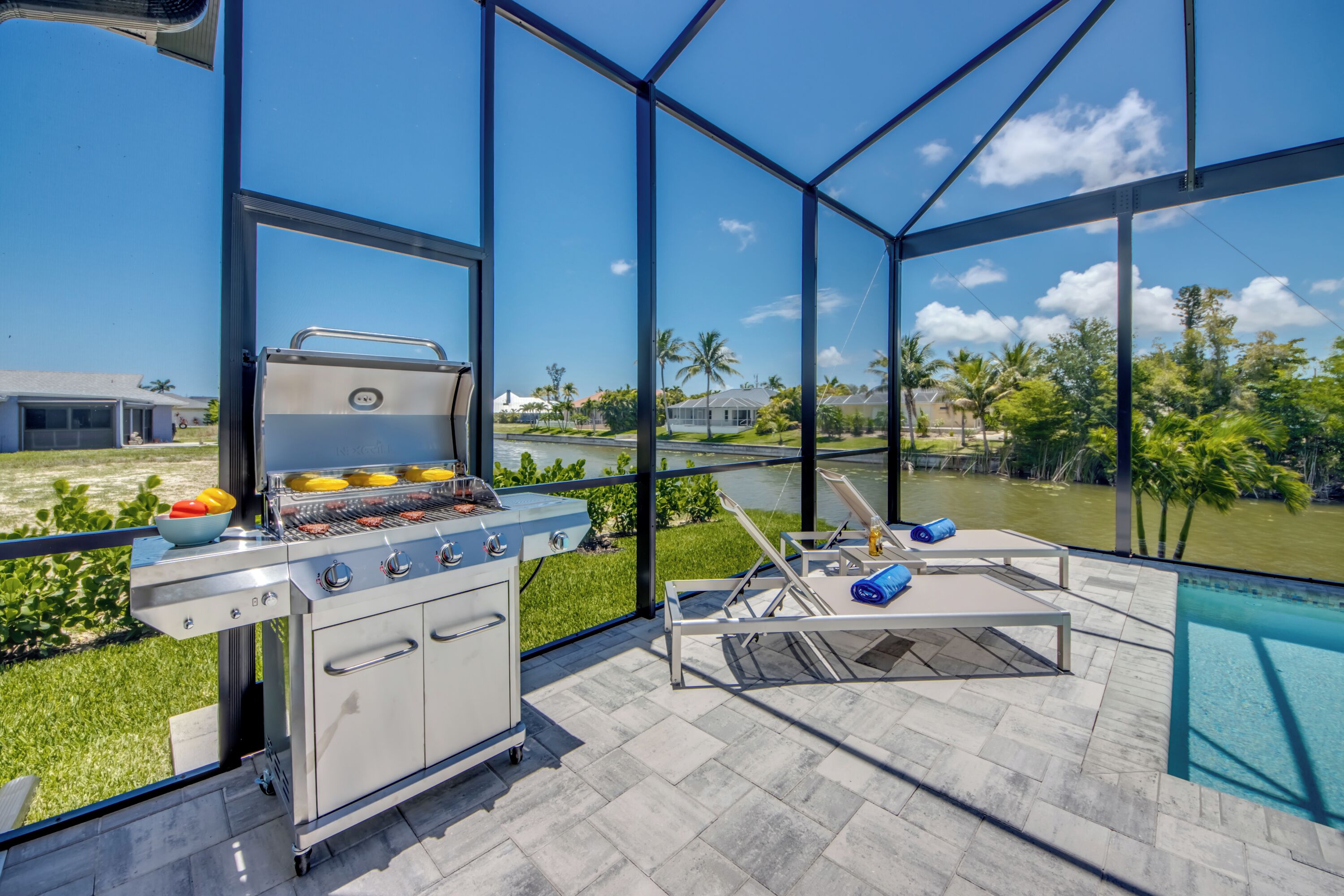 Eine moderne Außenküche mit Grill, eine Lounge-Bereich am Pool und Blick auf eine Wohngegend.