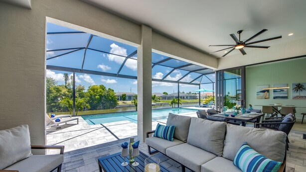 A spacious living area with a large glass door leading to a pool, a ceiling fan, and a comfortable seating arrangement. - Villa Sunrays -NEW 3-bedroom Villa with pool & spa (Cape Coral)