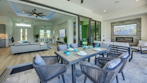 A modern living room with a dining area, a ceiling fan, a fireplace, and a TV mounted on the wall. - Villa Sunrays -NEW 3-bedroom Villa with pool & spa (Cape Coral)