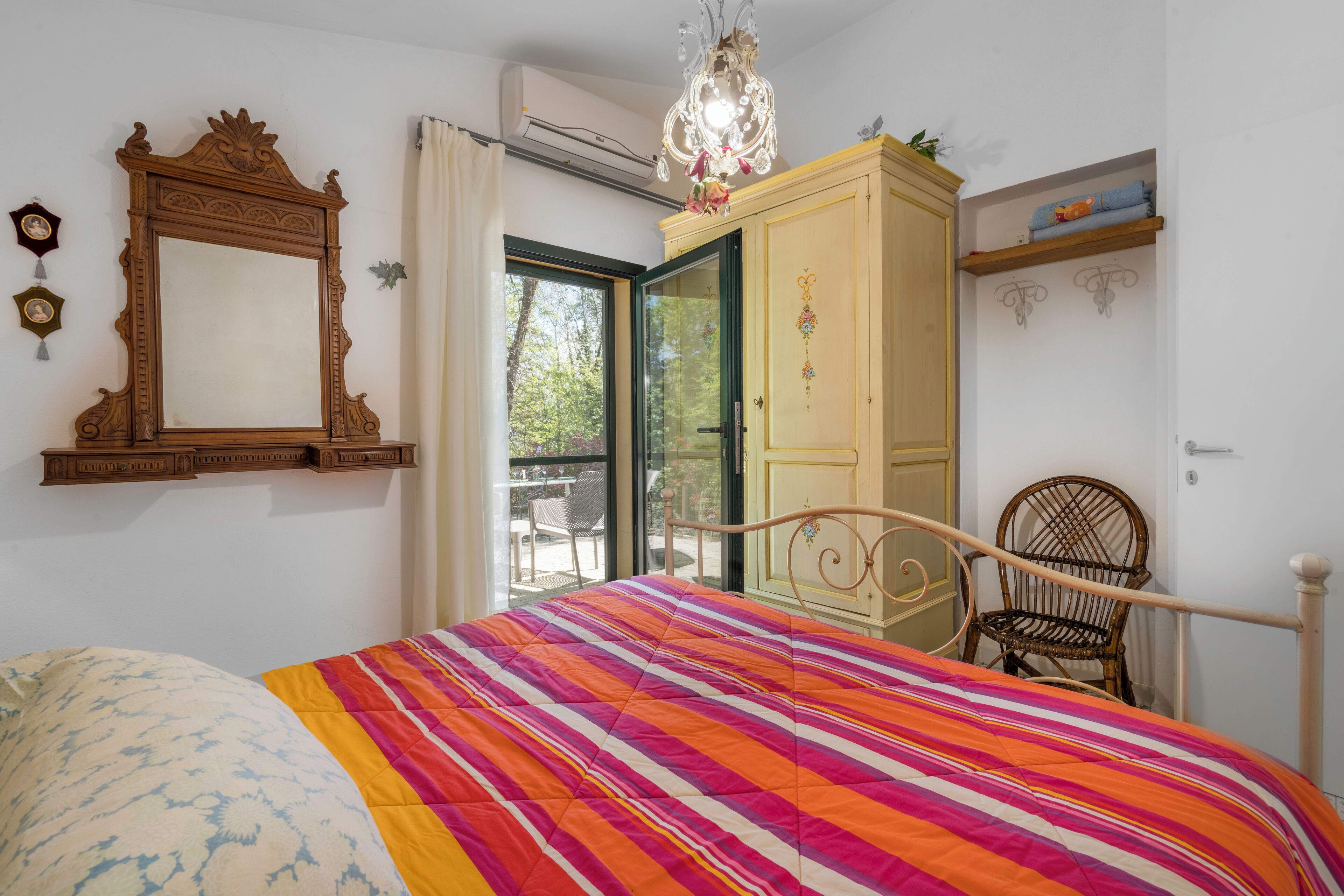 A bedroom with a bed, a wooden wardrobe, a chair, and a large mirror.