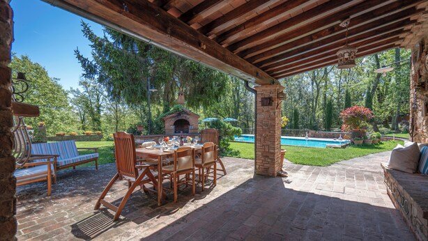 An outdoor patio with a brick table and chairs, a stone fireplace, and a pool in the background. - Grace Home Pool Wifi Gambassi Terme (Gambassi Terme)