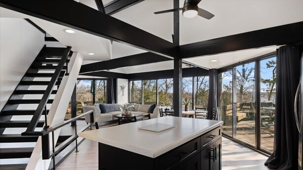 A modern kitchen with a central island, a staircase, and a dining area with outdoor views.