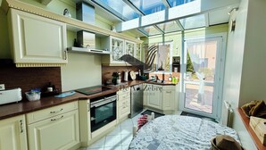 A kitchen with a large window, a dining area with a patterned tablecloth, and a view of the outside. - Le Ferney - Close to downtown and the spa (Rochefort)