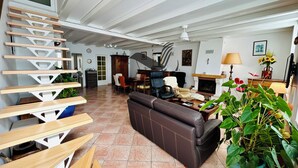A spacious living room with a fireplace, a sofa, a dining area, and a staircase. - Le Ferney - Close to downtown and the spa (Rochefort)