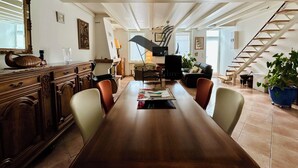 A spacious dining area with a long wooden table, surrounded by chairs, and a staircase leading to an upper level. - Le Ferney - Close to downtown and the spa (Rochefort)