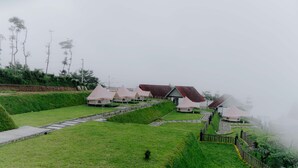 A series of tents with red roofs arranged on a grassy slope, connected by stone pathways. - Glamping Telaga Menjer By Travelink (Garung)