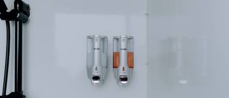 Two wall-mounted dispensers, one for soap and one for shampoo, in a bathroom.