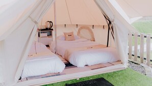 A tent with two beds, a small table with a kettle, and a black mat on the grass. - Glamping Telaga Menjer By Travelink (Garung)