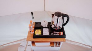 A small wooden table with a kettle, sugar packets, a bottle of water, and a box of tea. - Glamping Telaga Menjer By Travelink (Garung)