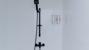A shower area with a handheld showerhead, a wall-mounted faucet, and two soap dispensers. - Glamping Telaga Menjer By Travelink (Garung)