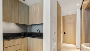 A modern kitchen with wooden cabinets, a black countertop, and a kettle. - Chic Studio with Pool Access in The Autograph (Dubai)